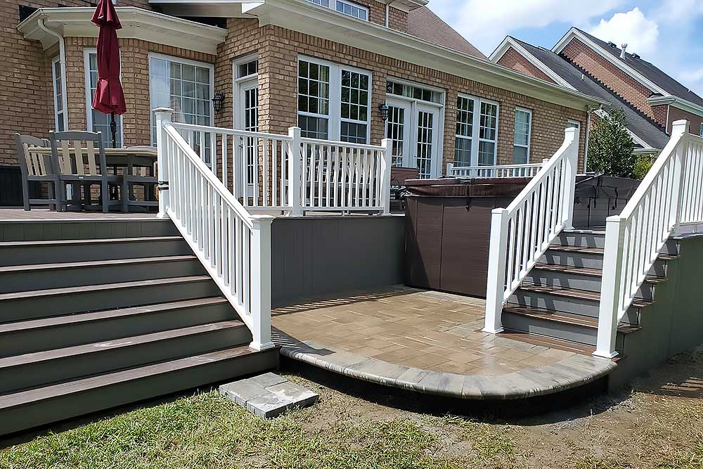 A spacious custom deck installation with white railings and brown steps, featuring outdoor furniture and a hot tub, exemplifies high-quality craftsmanship and enhances outdoor living in Virginia Beach.| First In Decks and Fencing | Virginia Beach Deck Builders