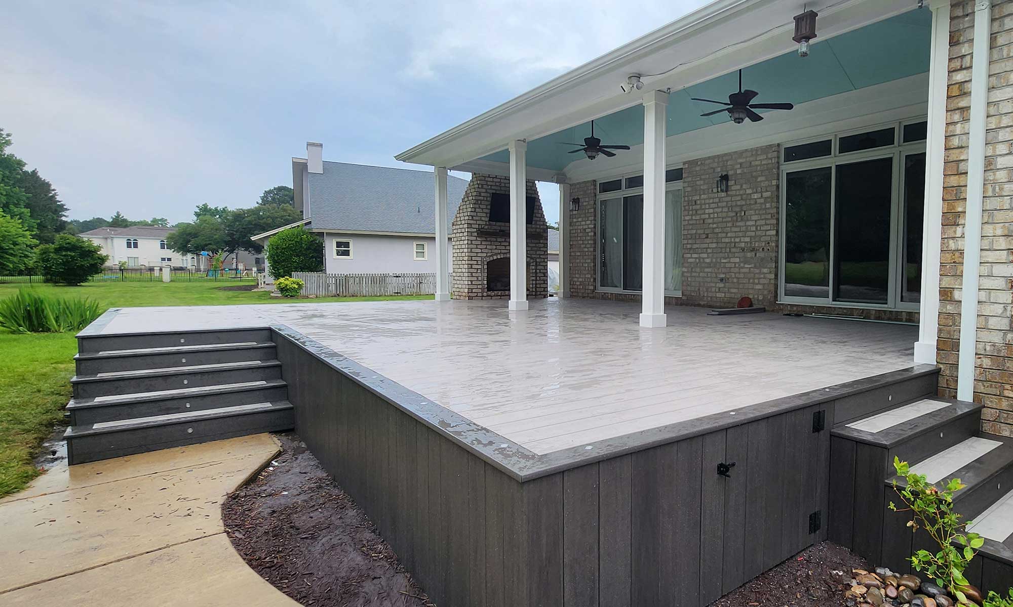 A spacious backyard with a custom deck installation featuring composite decking and an outdoor fireplace, showcasing professional craftsmanship and durable materials, perfect for enhancing outdoor living in Virginia Beach.| First In Decks and Fencing | Virginia Beach Deck Builders