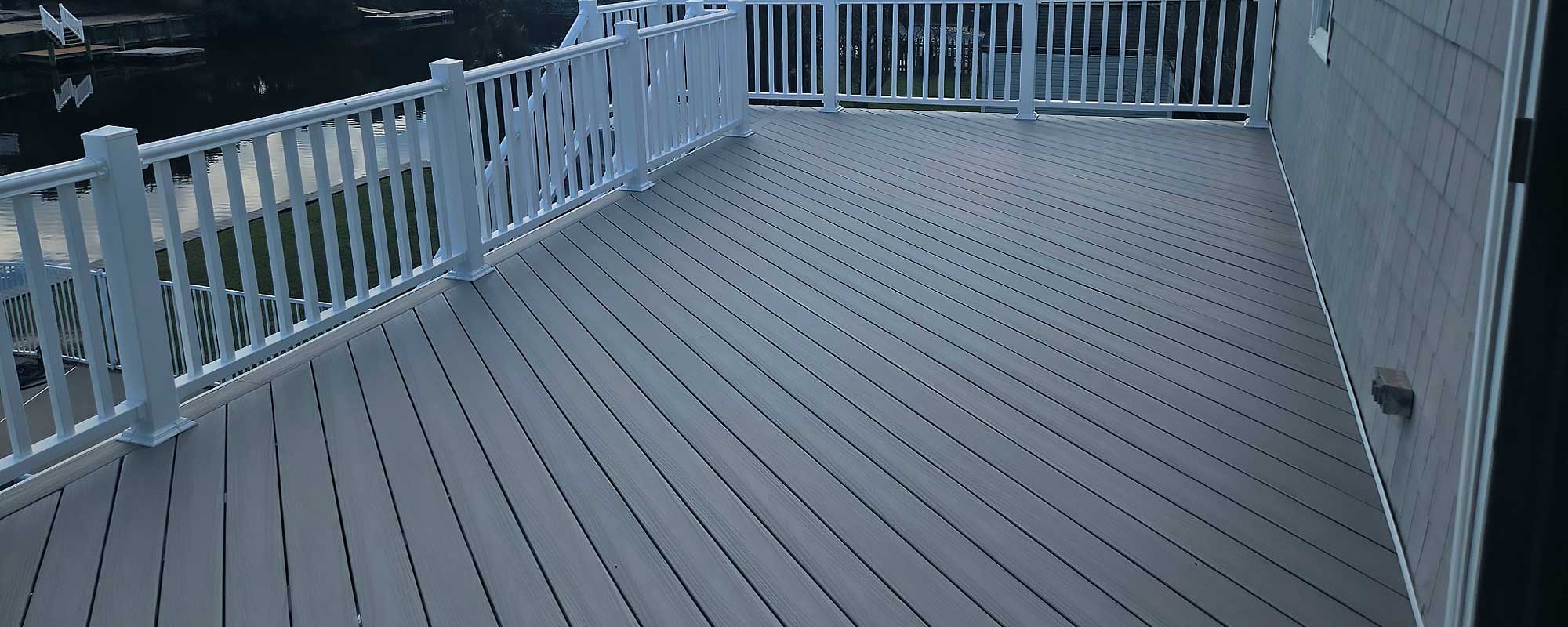 A spacious deck made of high-quality, low-maintenance composite decking with white railings overlooks a serene water view, ideal for enhancing outdoor living spaces in Chesapeake.| First In Decks and Fencing | Virginia Beach Deck Builders