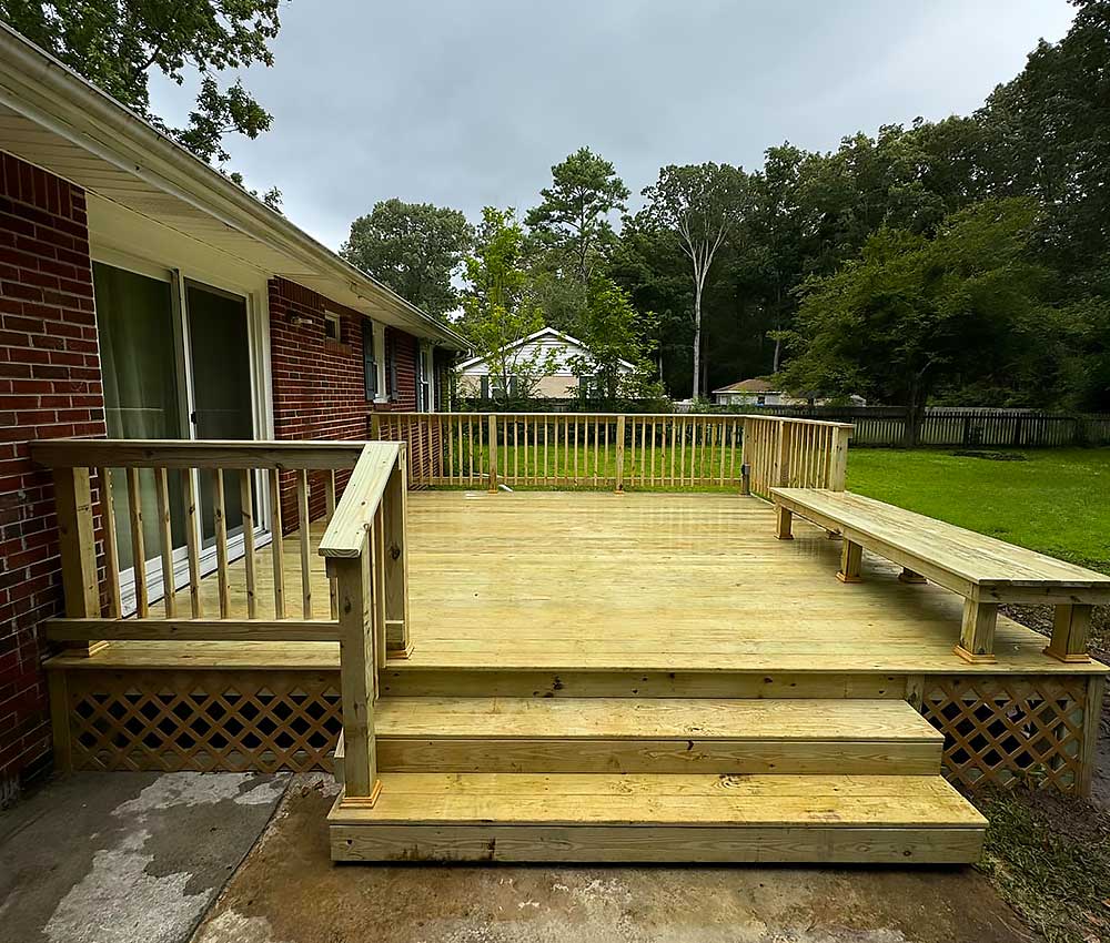 A newly constructed wooden deck with railing and built-in bench, showcasing professional craftsmanship using durable materials for outdoor living, set against a lush green backyard.| First In Decks and Fencing | Virginia Beach Deck Builders