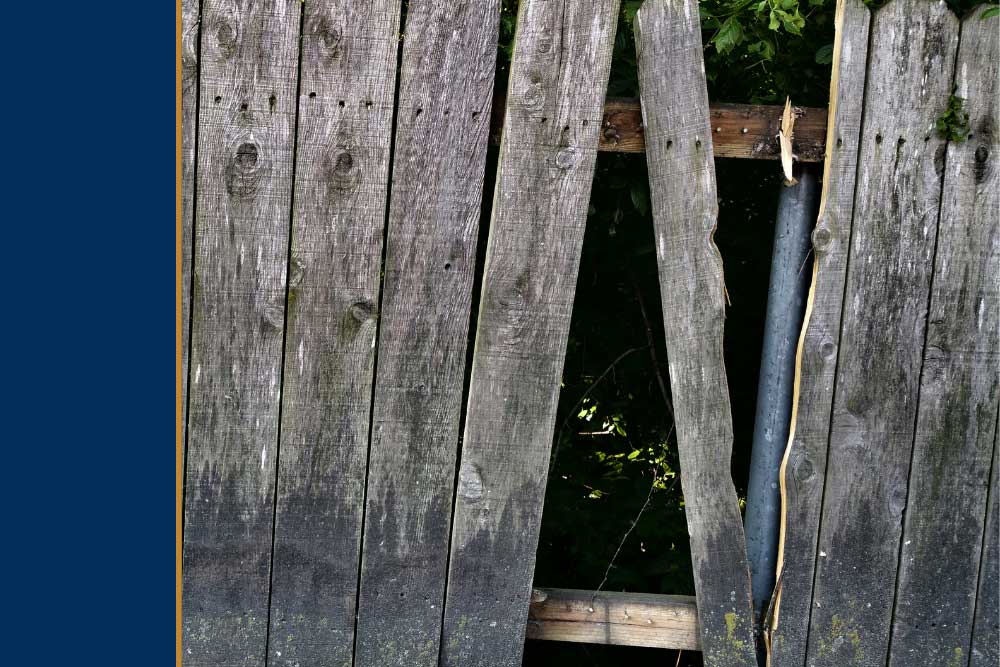Old, weathered wooden fence with missing planks, creating gaps. The fence appears in need of repair or replacement, highlighting the importance of dependable service and professional craftsmanship in fence repair and outdoor living improvements.| First In Decks and Fencing | Virginia Beach Deck Builders