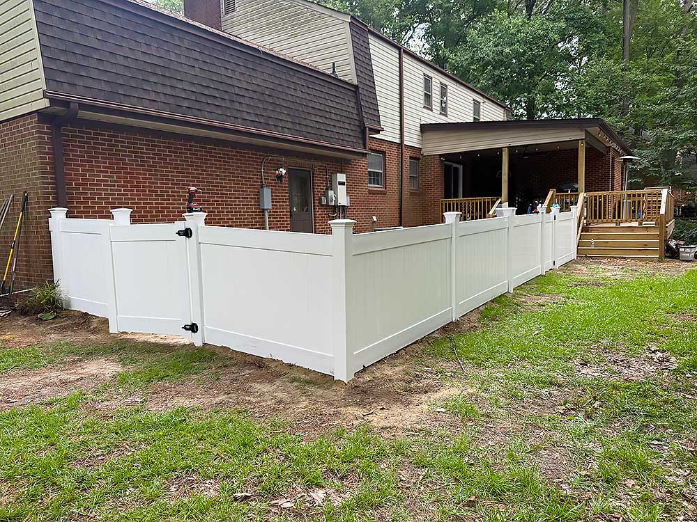 White vinyl privacy fence installed around a backyard with a deck, offering security and aesthetic appeal.