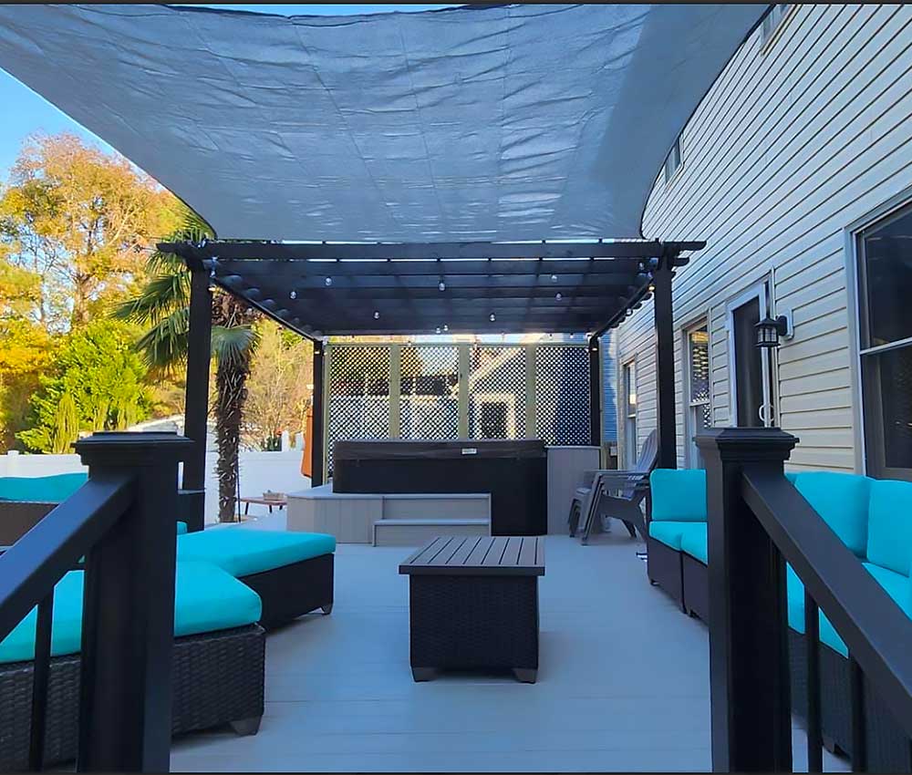 A spacious backyard deck in Virginia Beach features a pergola, comfortable seating with blue cushions, and a hot tub, showcasing high-quality, low-maintenance outdoor living with a focus on professional craftsmanship and backyard transformation.| First In Decks and Fencing | Virginia Beach Deck Builders