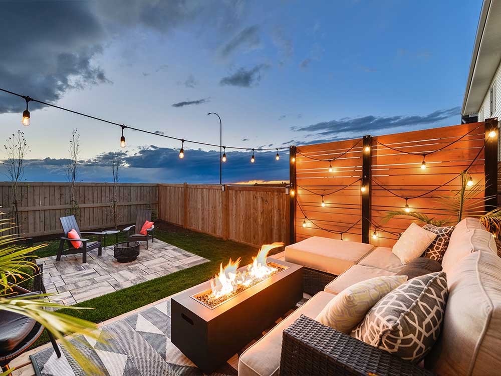 A cozy backyard features outdoor seating around a modern fire pit, with string lights above creating a warm ambiance. This inviting outdoor living space showcases…| First In Decks and Fencing | Virginia Beach Deck Builders