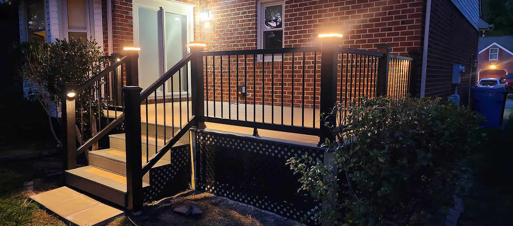 A well-lit custom deck installation features sleek railings and steps, surrounded by greenery, highlighting outdoor living with durable materials for a comfortable and stylish backyard transformation.| First In Decks and Fencing | Virginia Beach Deck Builders