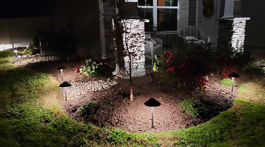 A beautifully lit garden at night features a small tree and vibrant flowers, surrounded by solar lights. The scene exemplifies outdoor living, highlighting high-quality, durable materials used for creating welcoming home improvement spaces.| First In Decks and Fencing | Virginia Beach Deck Builders