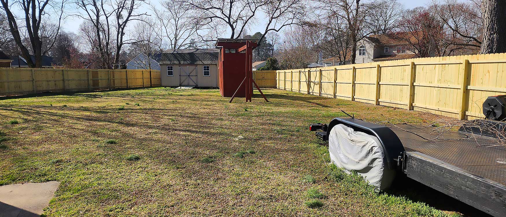 A spacious backyard features a well-maintained lawn, a wooden play structure, a large shed, and a new wooden fence installation, emphasizing outdoor living and home improvement with durable materials.| First In Decks and Fencing | Virginia Beach Deck Builders